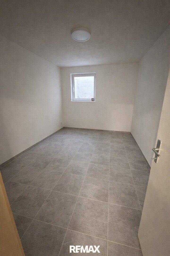 Einfaches Zimmer mit grauen Fliesen und kleinem Fenster, geeignet als Hobbyraum oder Lager.
