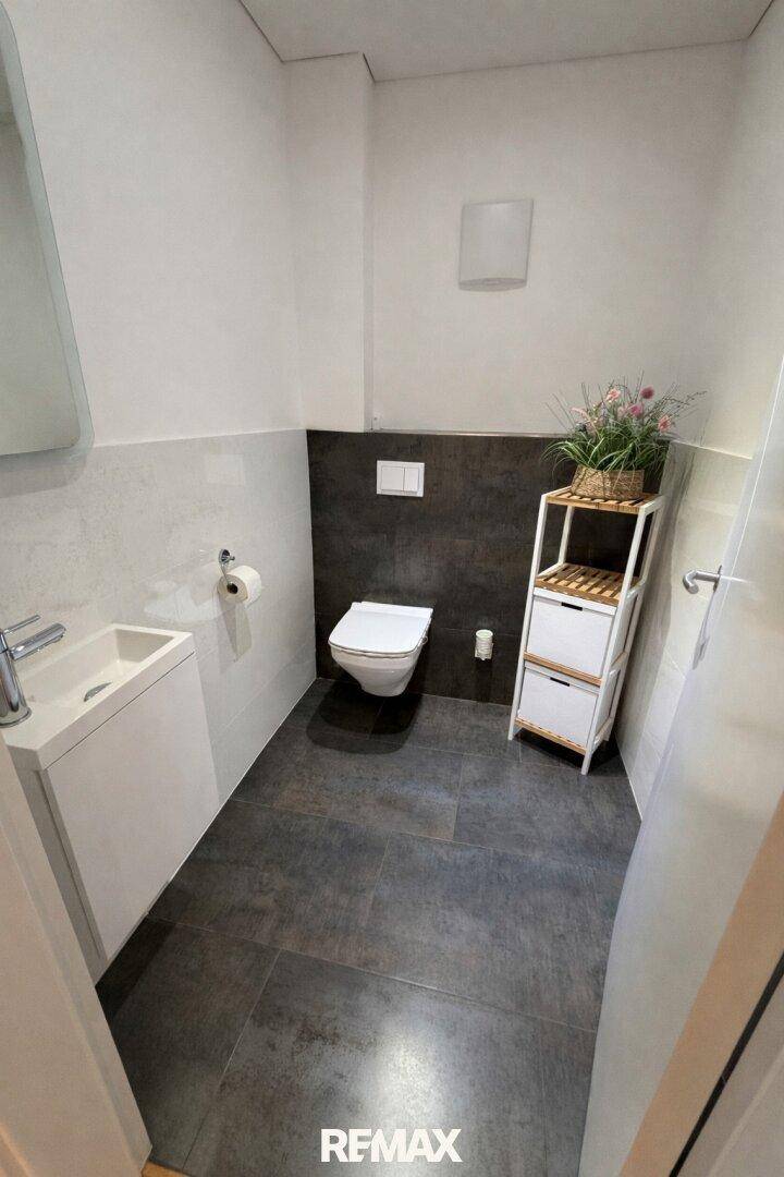 Praktisches Gäste-WC mit wandhängendem WC, modernem Waschbecken und dunklen Bodenfliesen.