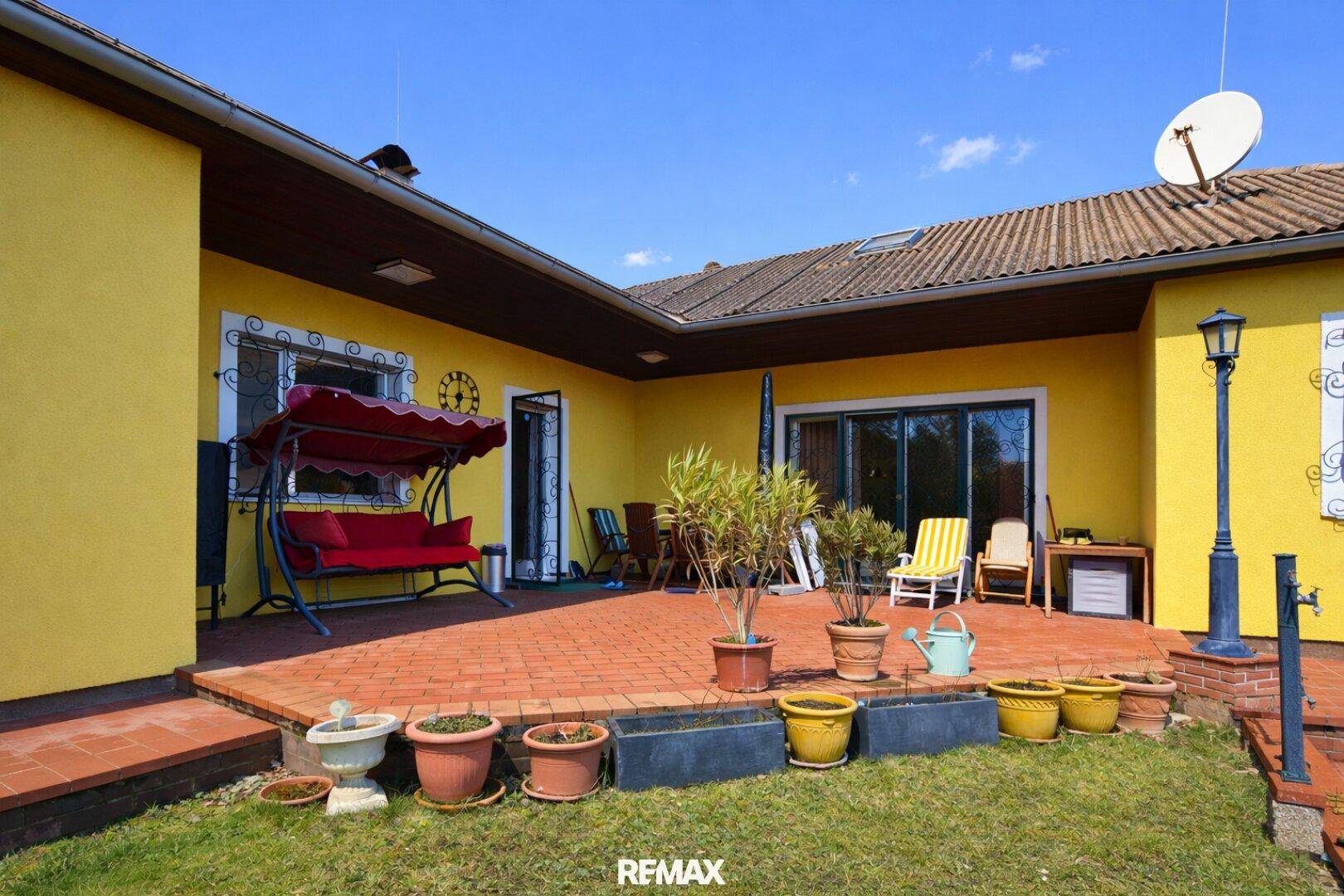 Große geflieste Terrasse mit Schaukelbank und Zugang zum Garten, ideal für Entspannung.