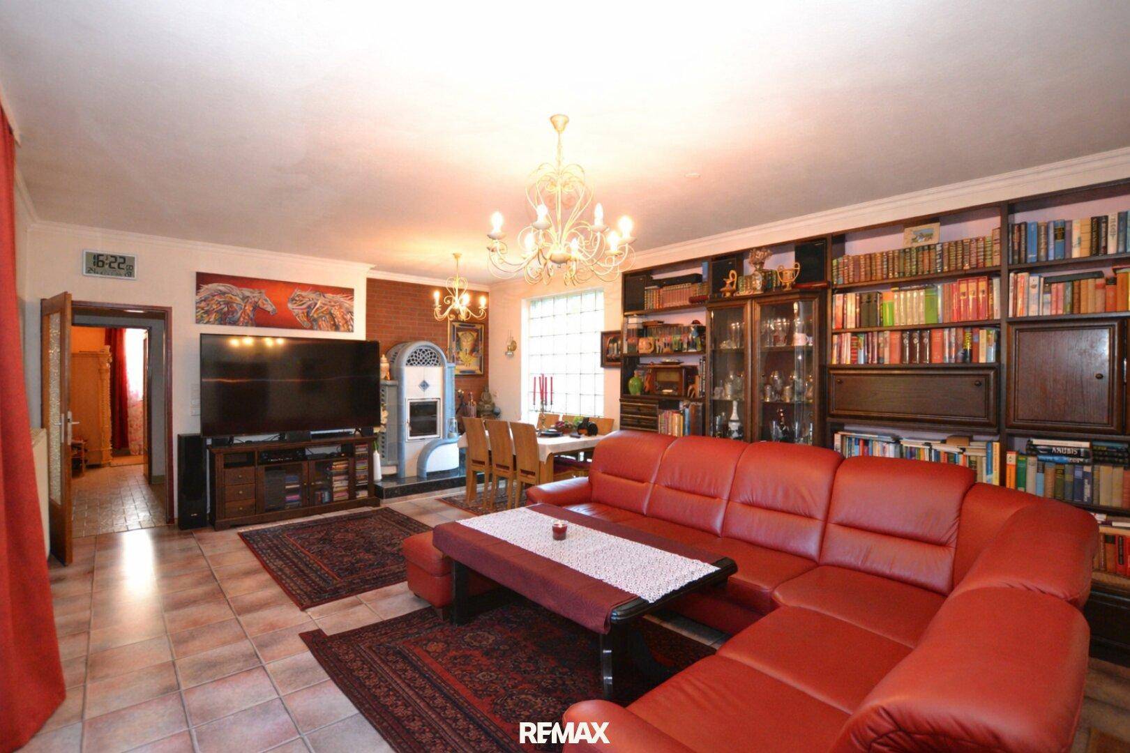 Geräumiger Wohn- und Essbereich mit großem Bücherregal, Kachelofen und rotem Sofa.