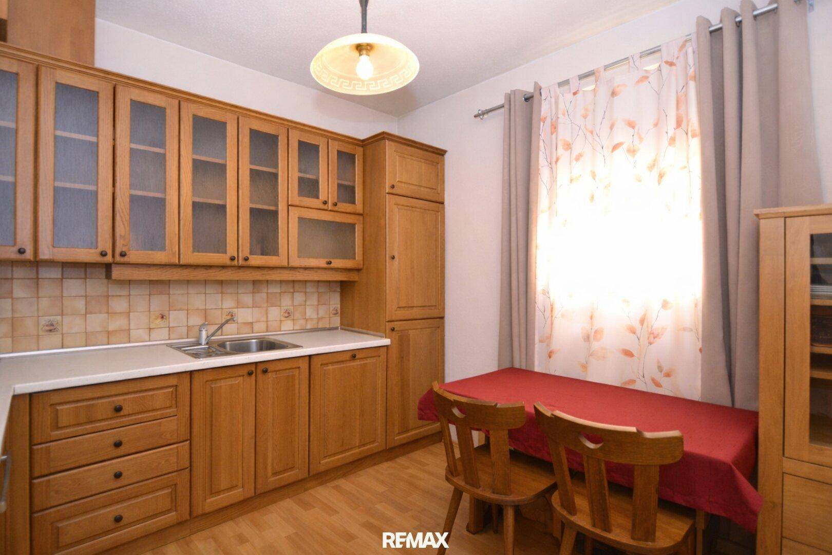 Gemütliche Küche mit Holzschränken, Essbereich und Fenster für natürliches Licht.
