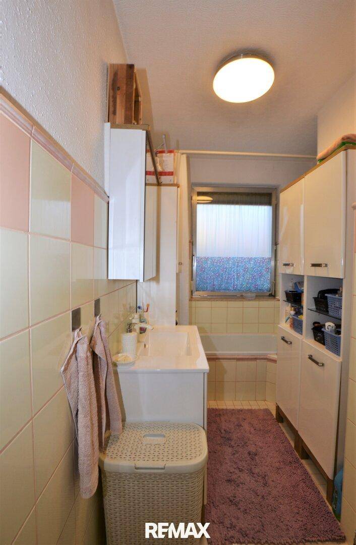 Badezimmer mit Badewanne, Waschbecken und hellen Fliesen in Pastellfarben.