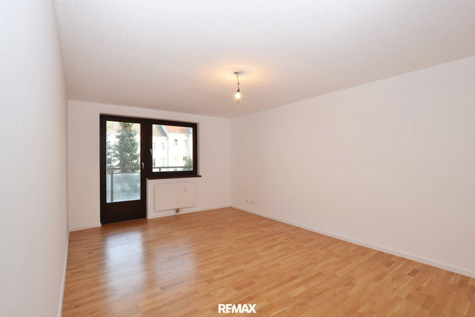 Geräumiger, leerer Raum mit Holzboden und Zugang zu einem Balkon.
