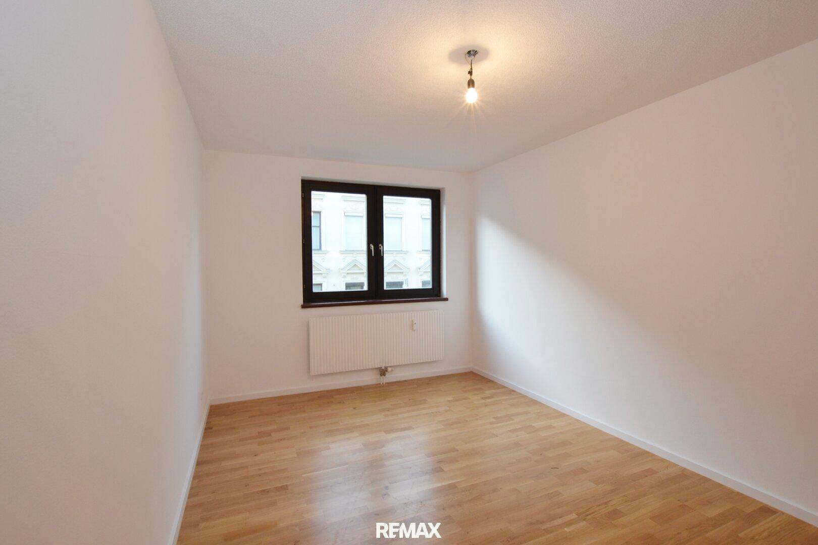 Leeres Schlafzimmer mit Holzboden und Fenster mit Blick auf die Stadt.