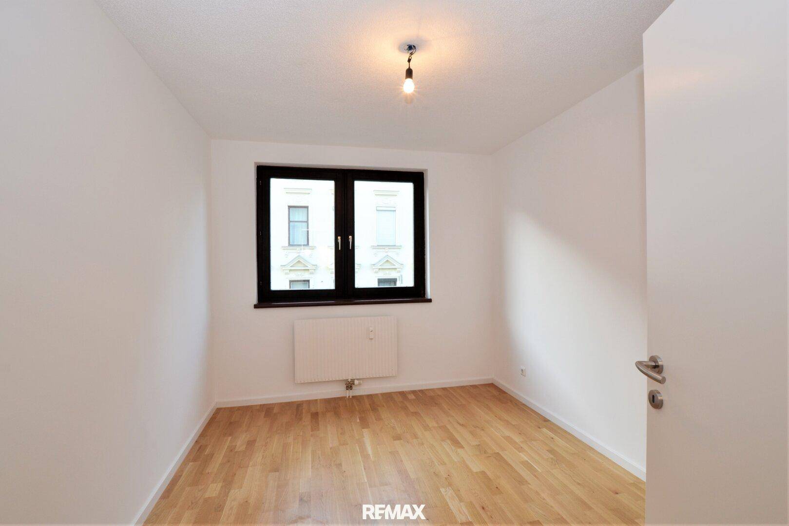 Leeres Schlafzimmer mit Holzboden und Fenster mit Blick auf die Stadt.