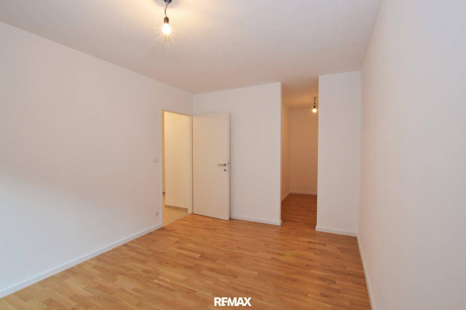 Geräumiger, leerer Raum mit Holzboden und Zugang zu einem weiteren Zimmer.
