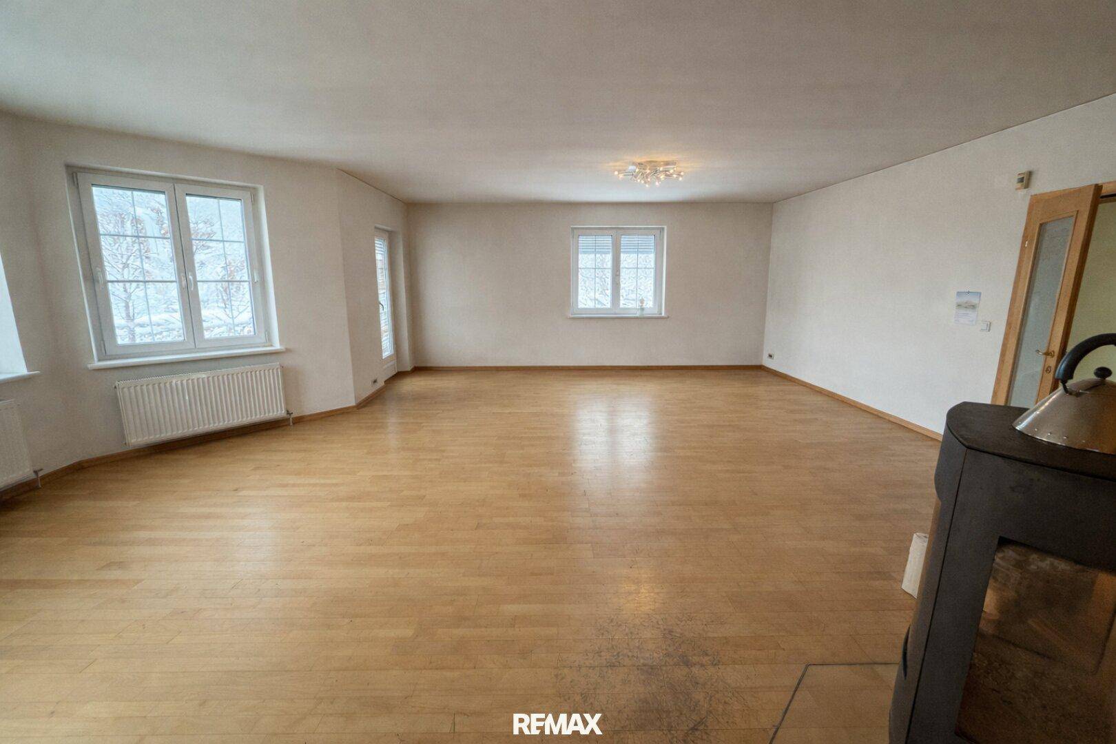 Geräumiges, leeres Wohnzimmer mit Holzboden, hellen Wänden und mehreren Fenstern.