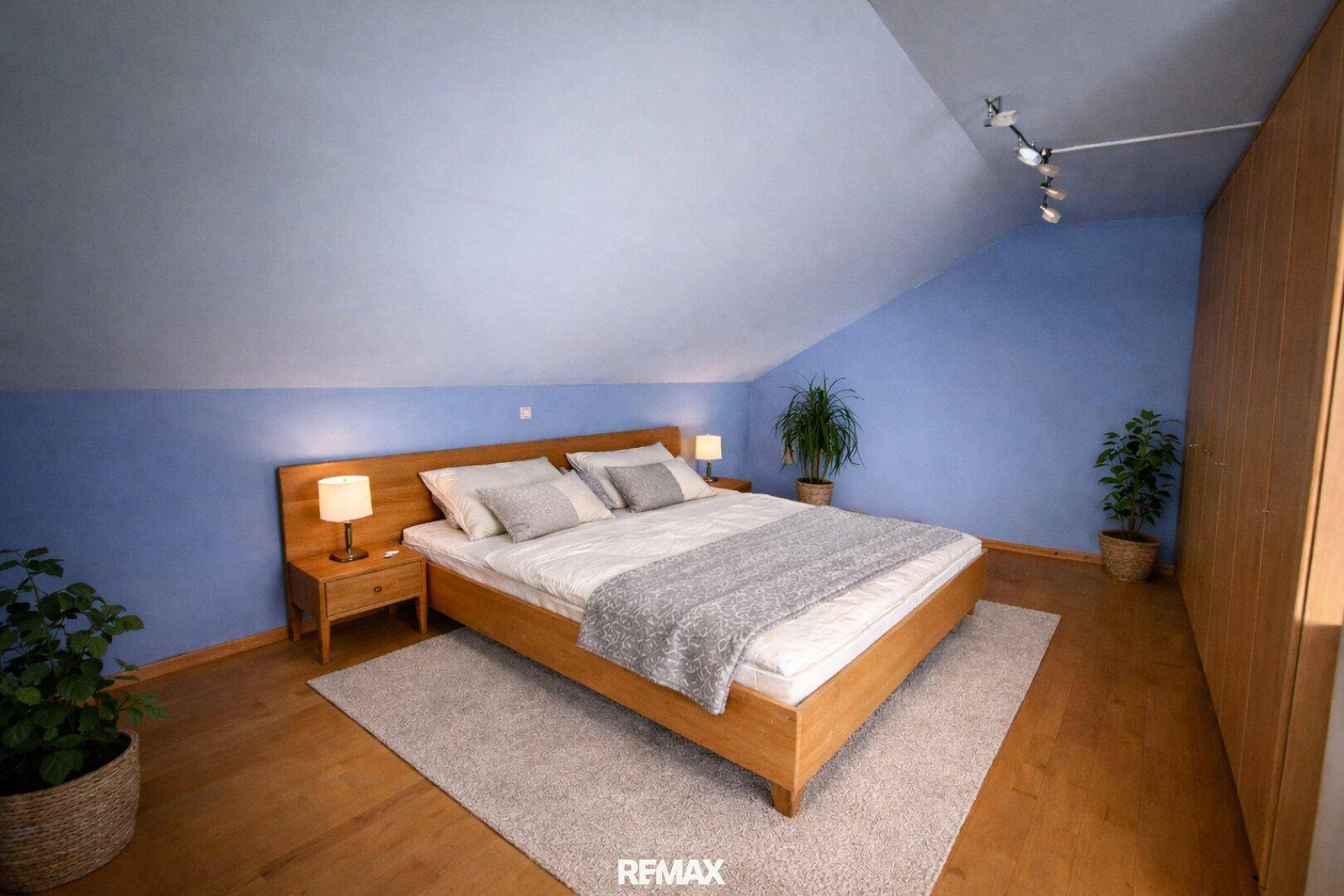 Gemütliches Schlafzimmer im Dachgeschoss mit Holzbett, blauen Wänden und Dachschräge.