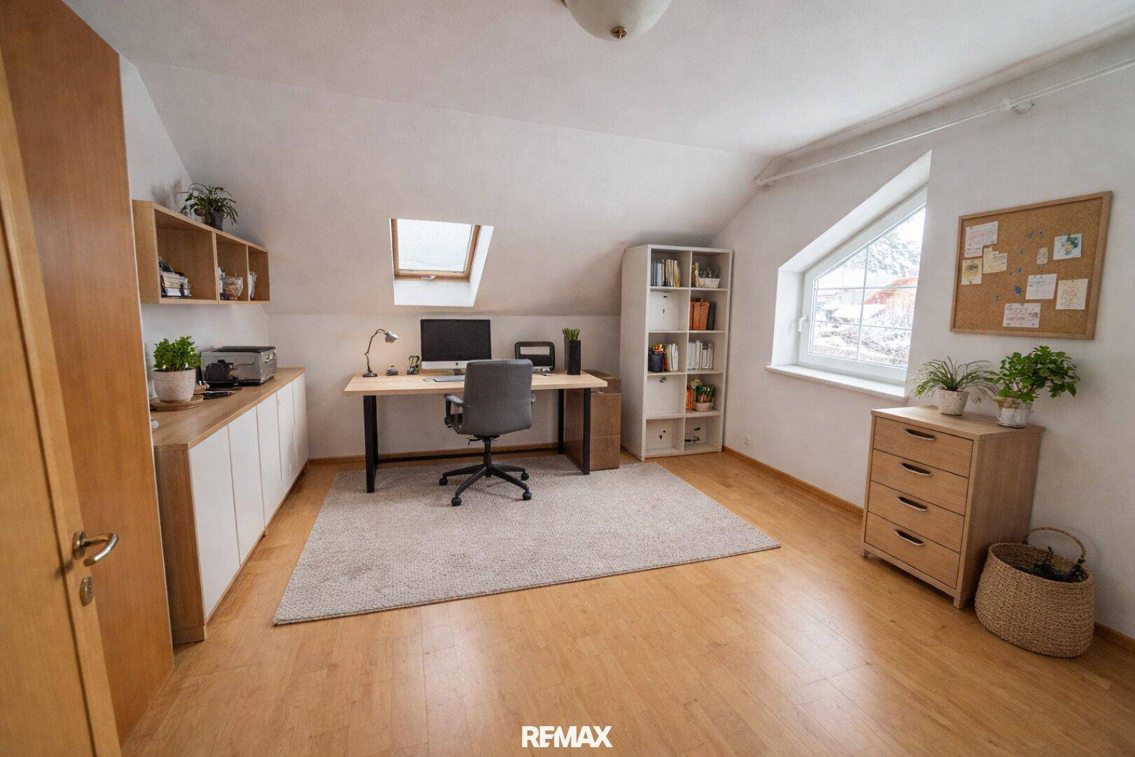 Helles Arbeitszimmer im Dachgeschoss mit Schreibtisch, Bücherregal und Dachfenster.