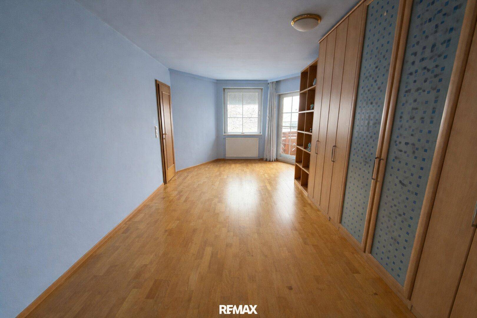 Leerer Raum mit Holzboden, blauen Wänden und einem großen Einbauschrank.