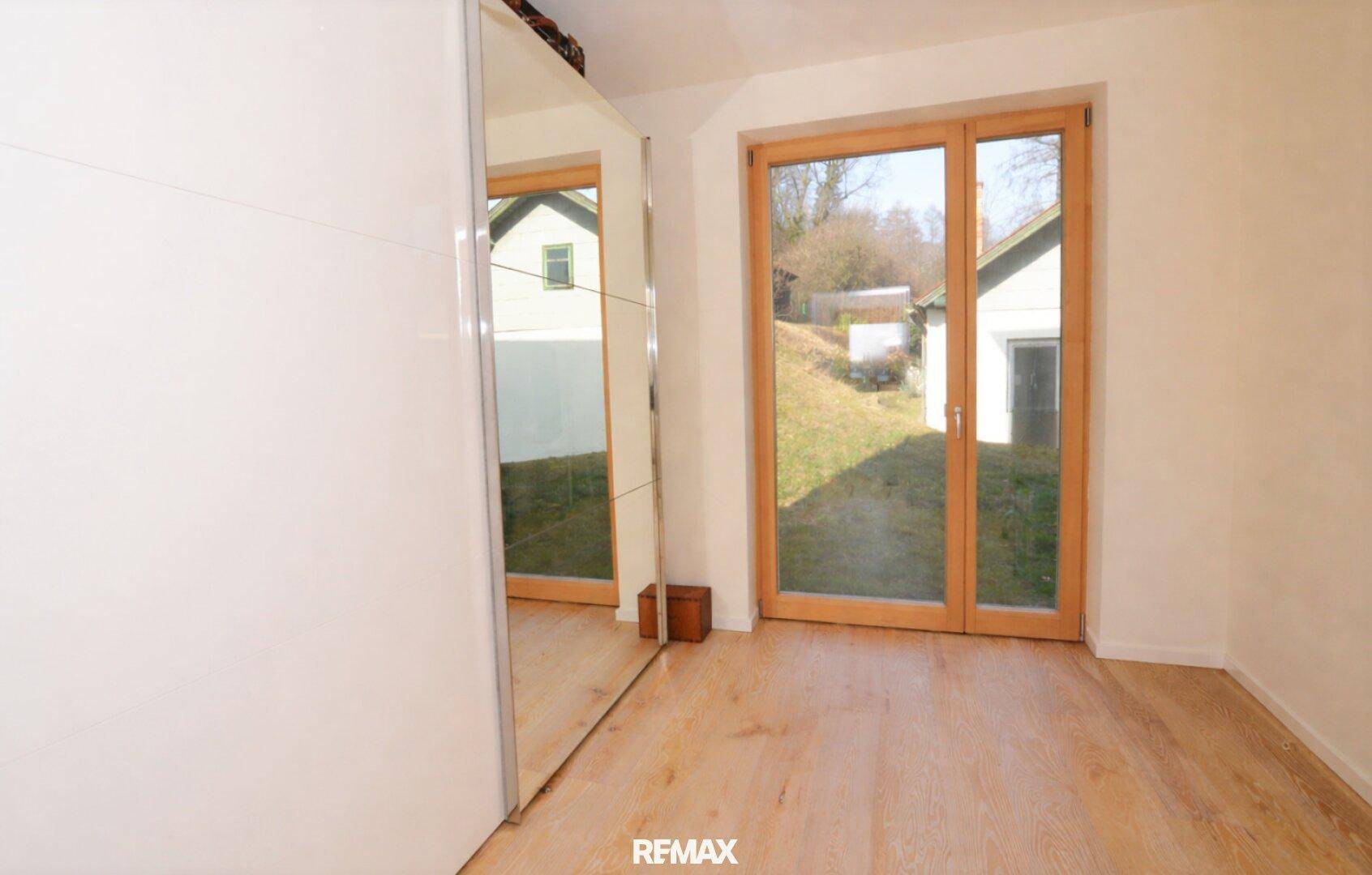 Schlafzimmer mit Parkettboden, Spiegelschrank und Zugang zum Garten durch eine Terrassentür.