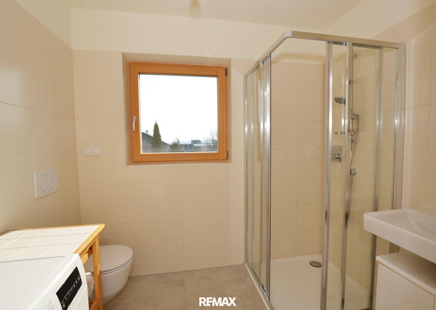 Helles Badezimmer mit Duschkabine, Toilette, Waschbecken und Fenster.