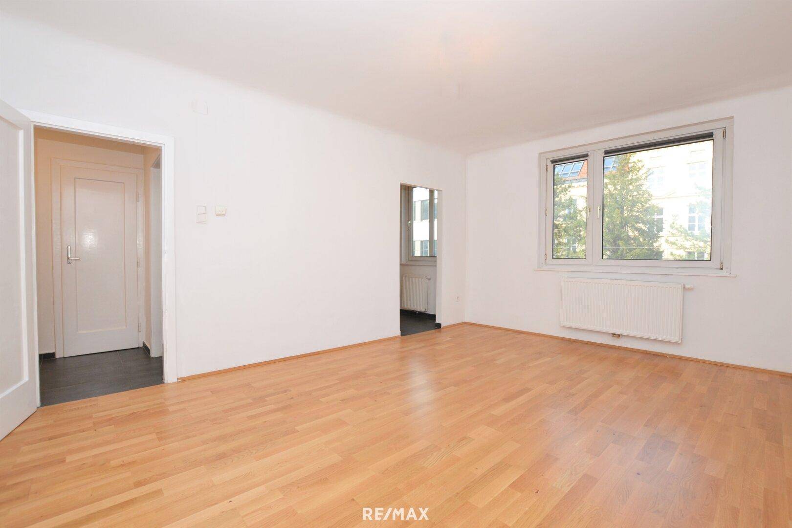 Geräumiges, leeres Wohnzimmer mit hellem Holzboden und großen Fenstern.