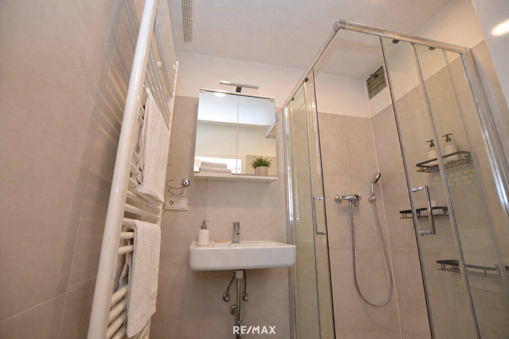 Modernes Badezimmer mit Duschkabine, Waschbecken und beheiztem Handtuchhalter.