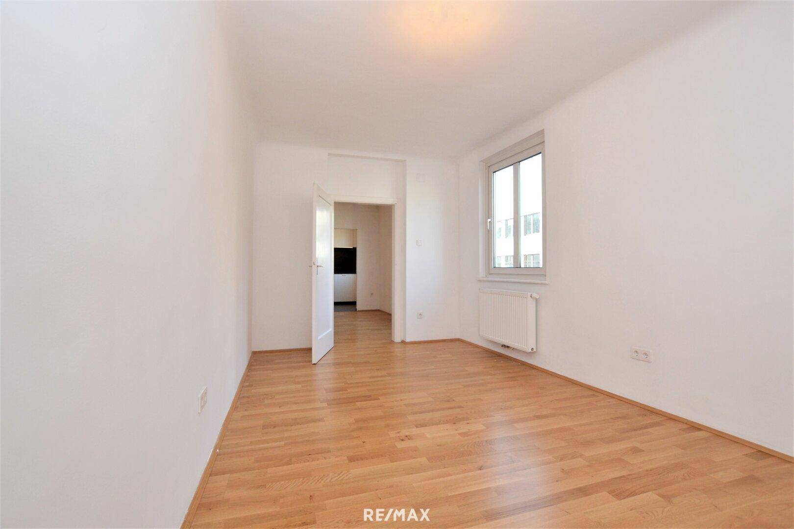 Leeres Kinderzimmer mit hellem Holzboden und Fenster.