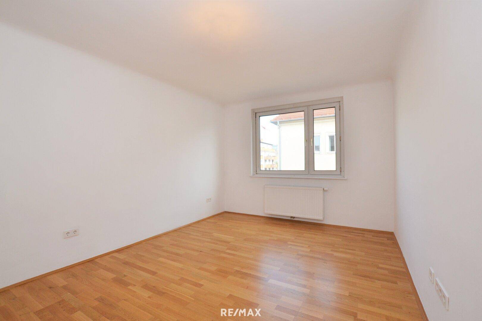 Leeres Schlafzimmer mit hellem Holzboden und Fenster mit Blick nach draußen.