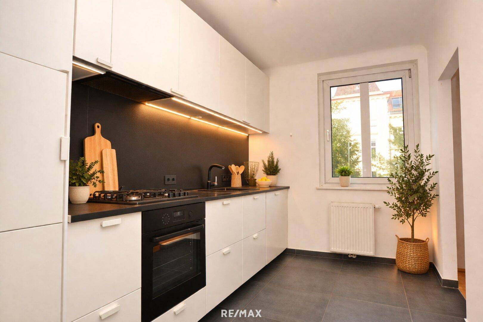 Moderne Küche mit weißen Schränken, dunkler Arbeitsplatte und Gasherd.