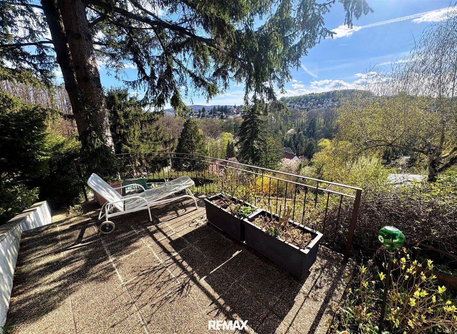 Sonniger Terrassenbereich mit Liegestuhl und Blumenkästen, bietet einen weiten Blick ins Grüne.