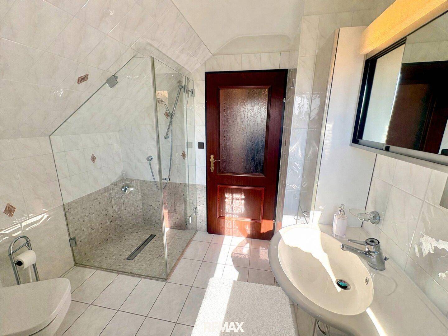 Helles Badezimmer mit weißen Fliesen, begehbarer Dusche und einem Waschbecken mit Spiegelschrank.