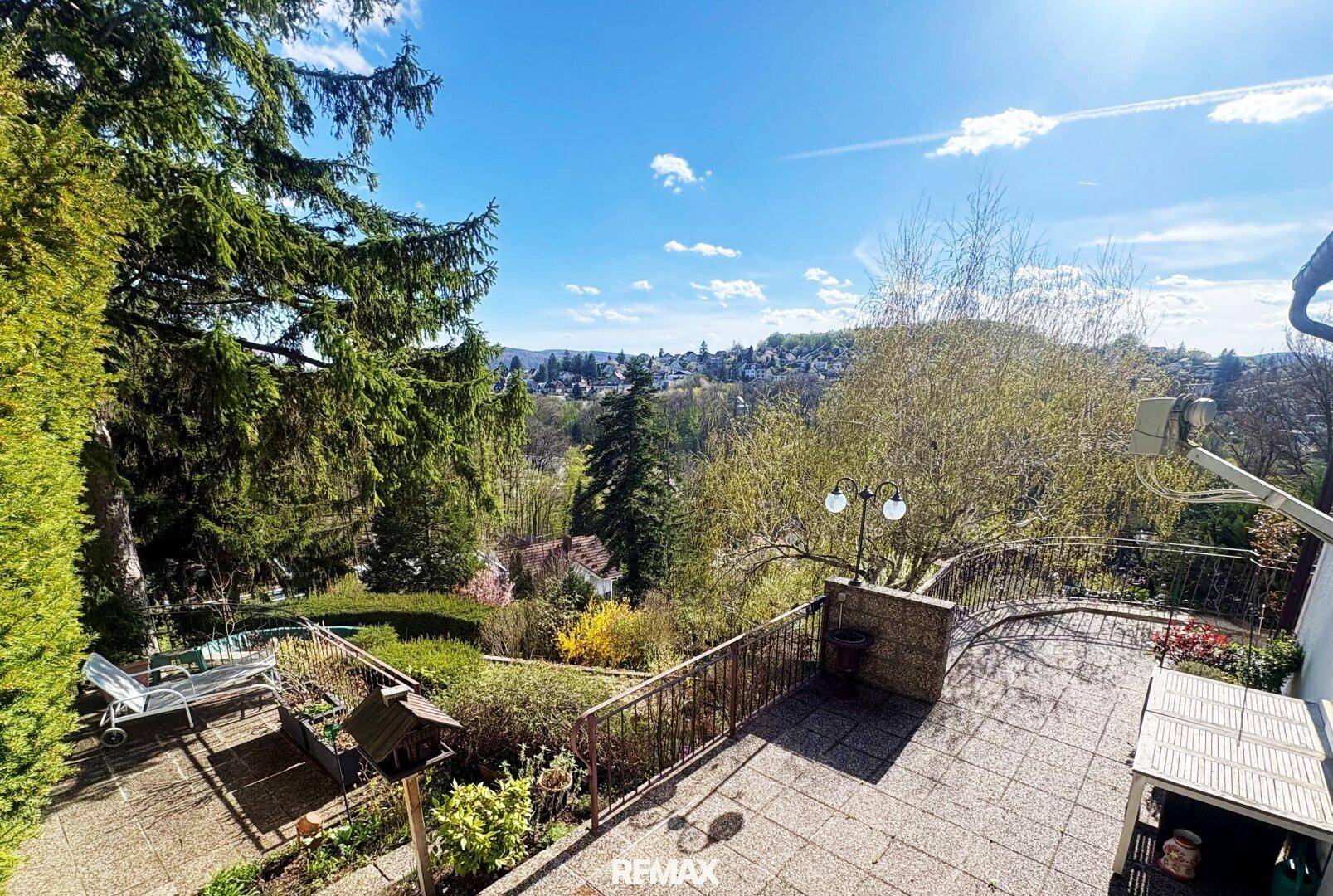 Große Terrasse mit weitem Blick über die grüne Landschaft und die umliegende Siedlung unter strahlendem Himmel.