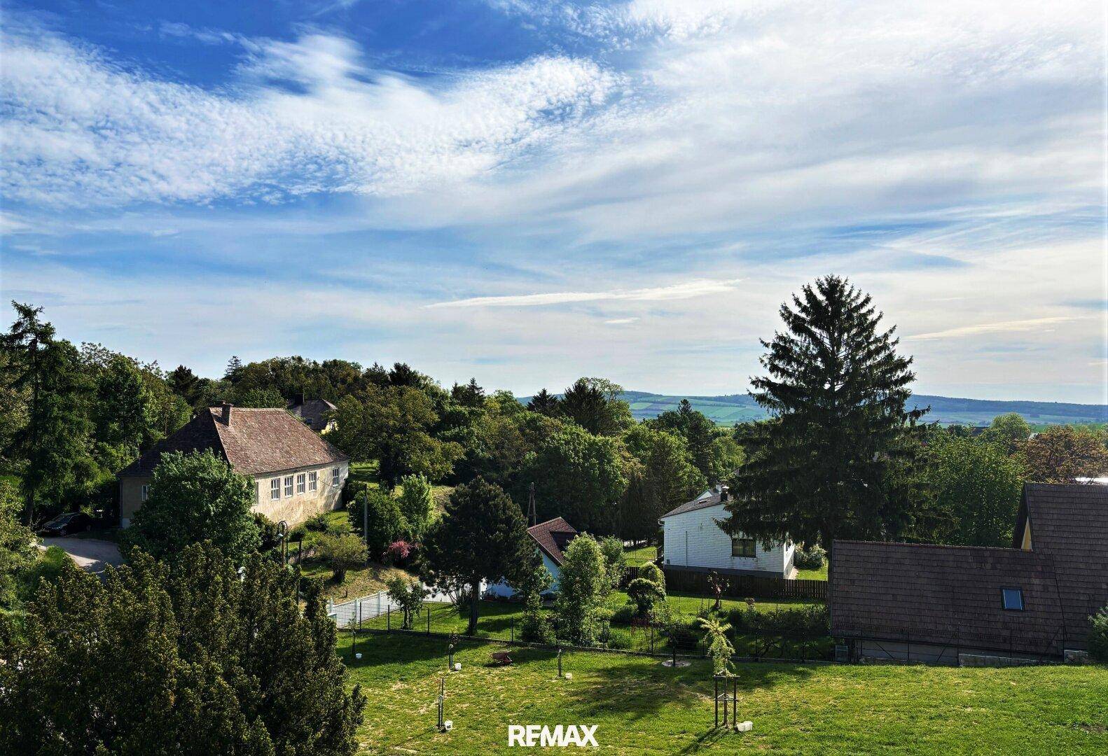 Panoramablick über eine grüne Hügellandschaft mit verstreuten Häusern und weitem Horizont.