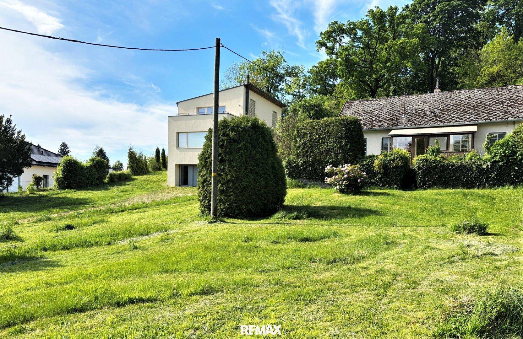 Modernes Haus in ländlicher Umgebung mit großem Garten und Blick auf benachbarte Gebäude.