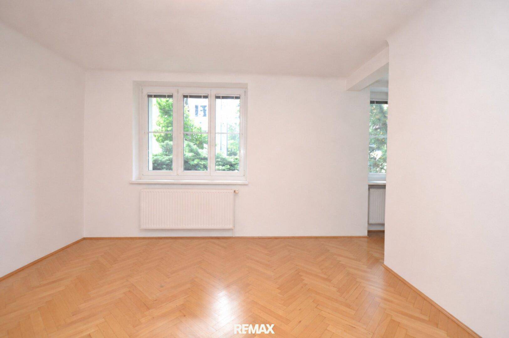 Helles, leeres Wohnzimmer mit Fischgrätparkett und großem Fenster, bereit zur individuellen Gestaltung.