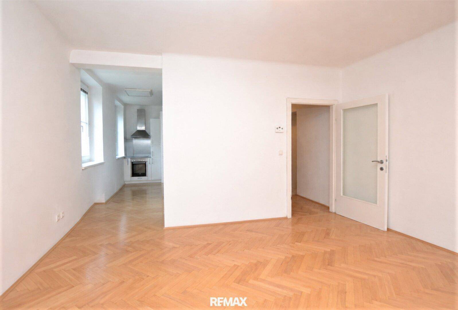 Leeres Wohnzimmer mit Parkettboden und Blick in die angrenzende Küche, ideal für offenes Wohnen.