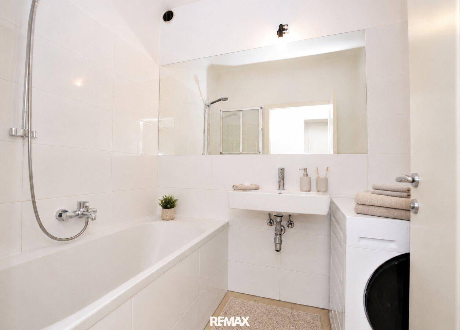 Modernes Badezimmer mit Badewanne, Waschbecken und Waschmaschine, komplett gefliest in Weiß.