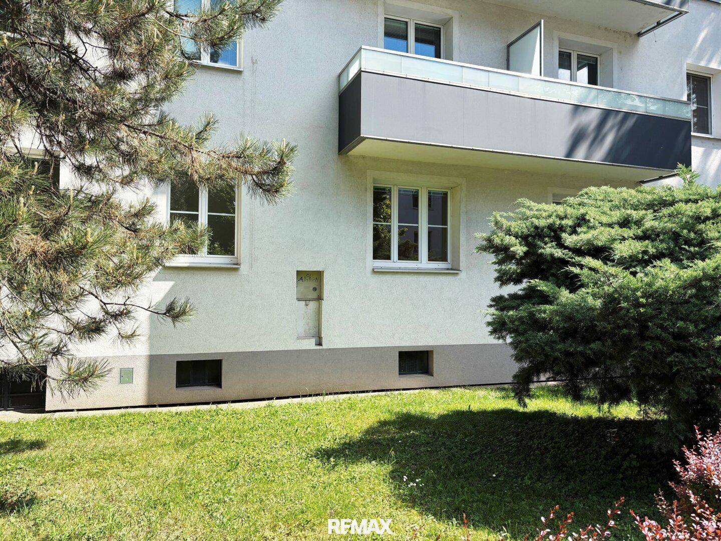 Außenansicht eines Wohngebäudes mit Balkon und gepflegter Grünfläche im Vordergrund.