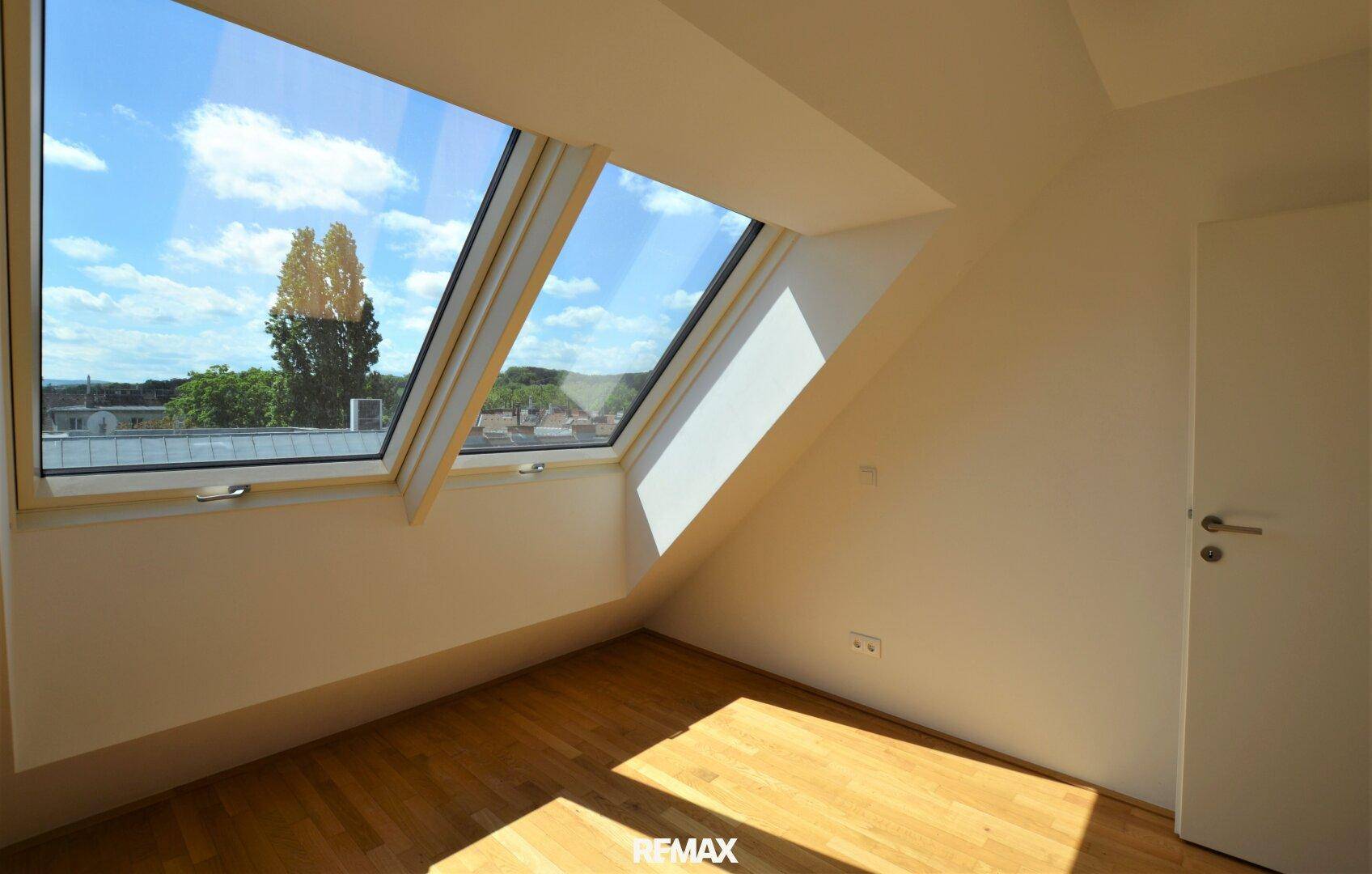 Helles Schlafzimmer mit Holzboden und großen Dachfenstern, die viel Tageslicht hereinlassen.