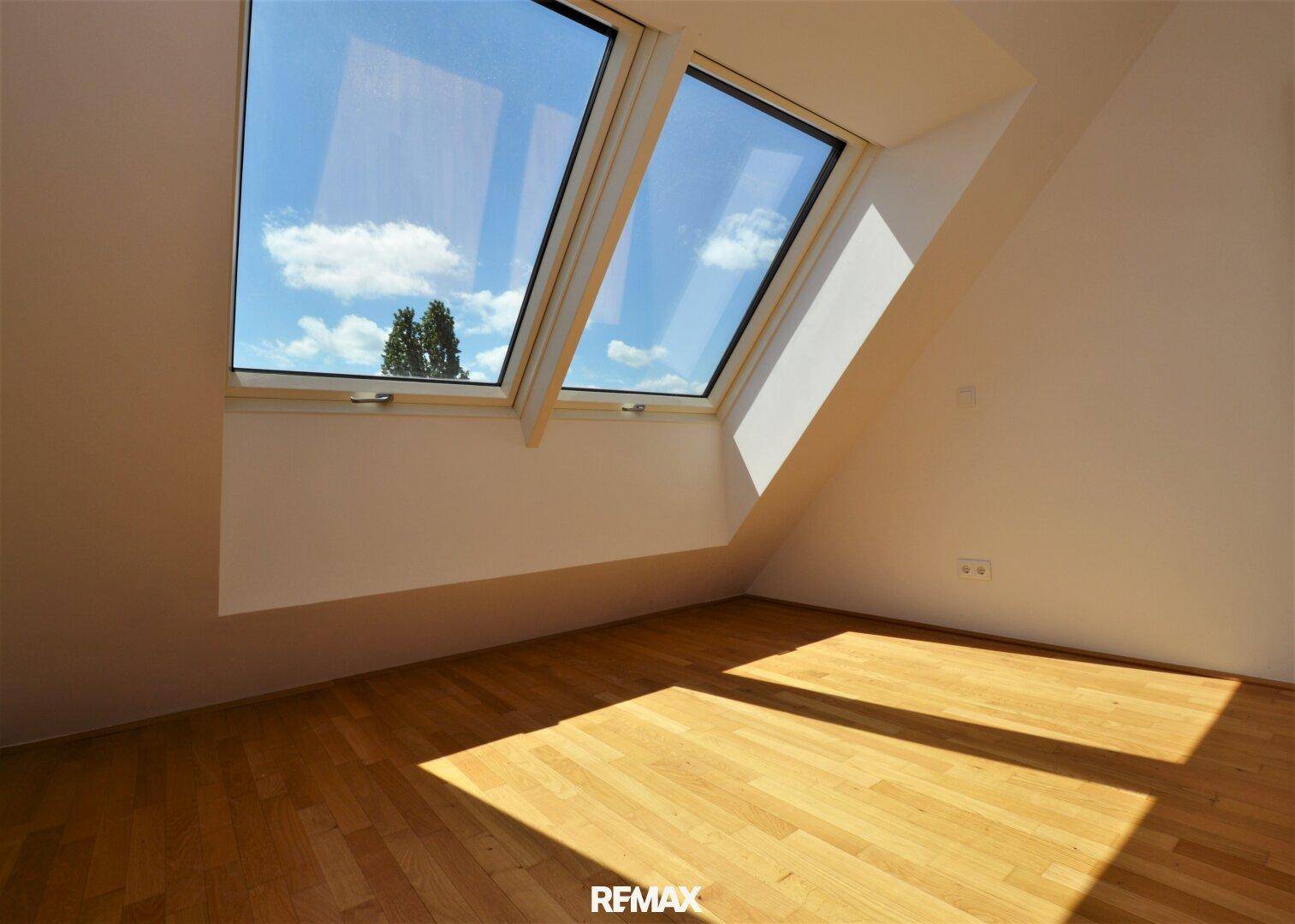 Unmöblierter Raum mit Holzboden und großen Dachfenstern, ideal als Büro oder Kinderzimmer.