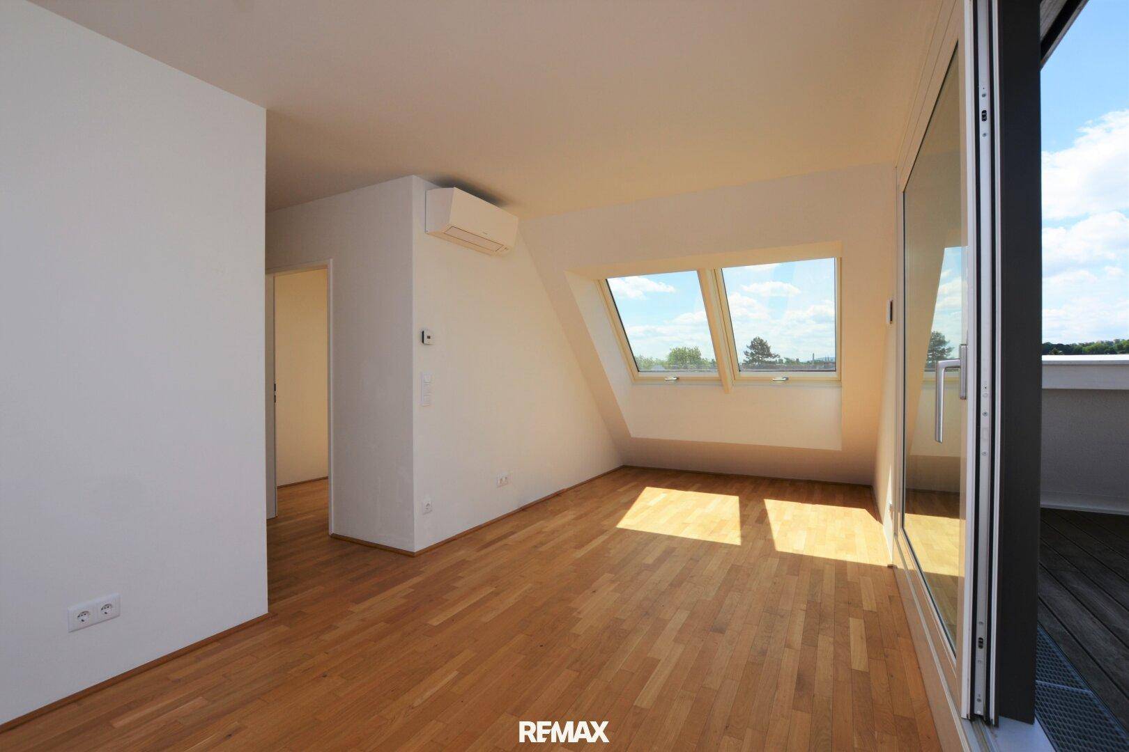 Geräumiger, unmöblierter Wohnbereich mit Holzboden, Klimaanlage und Zugang zur Dachterrasse.