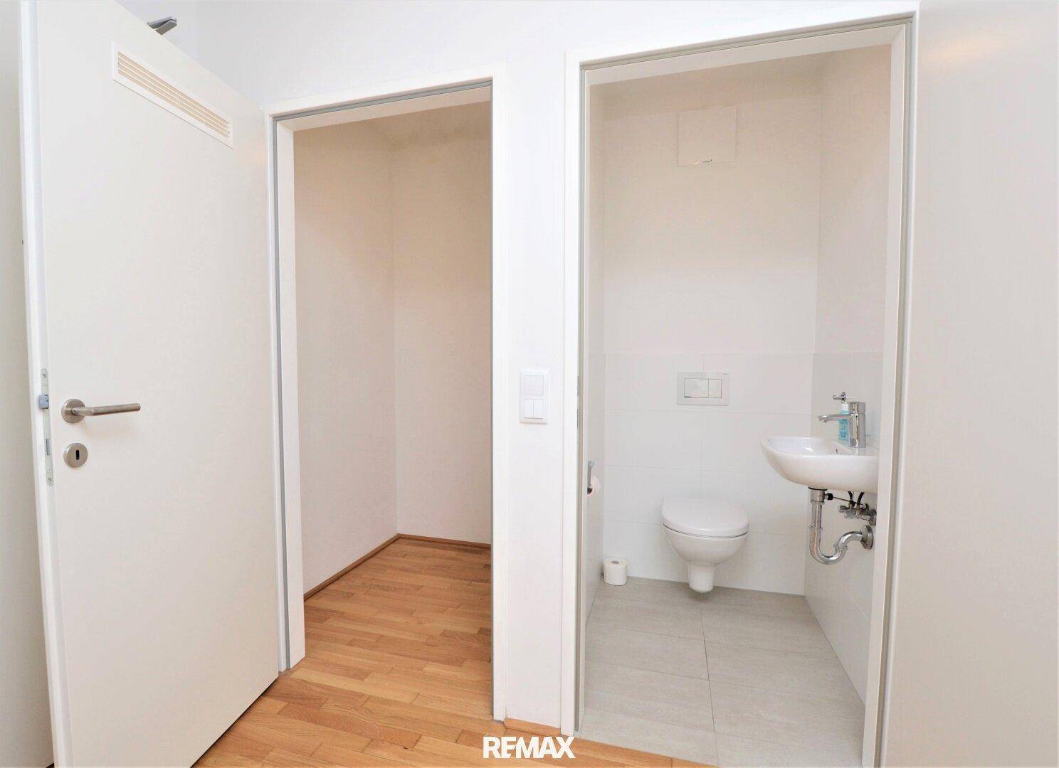 Kleines Gäste-WC mit Waschbecken und Toilette, daneben ein Abstellraum.