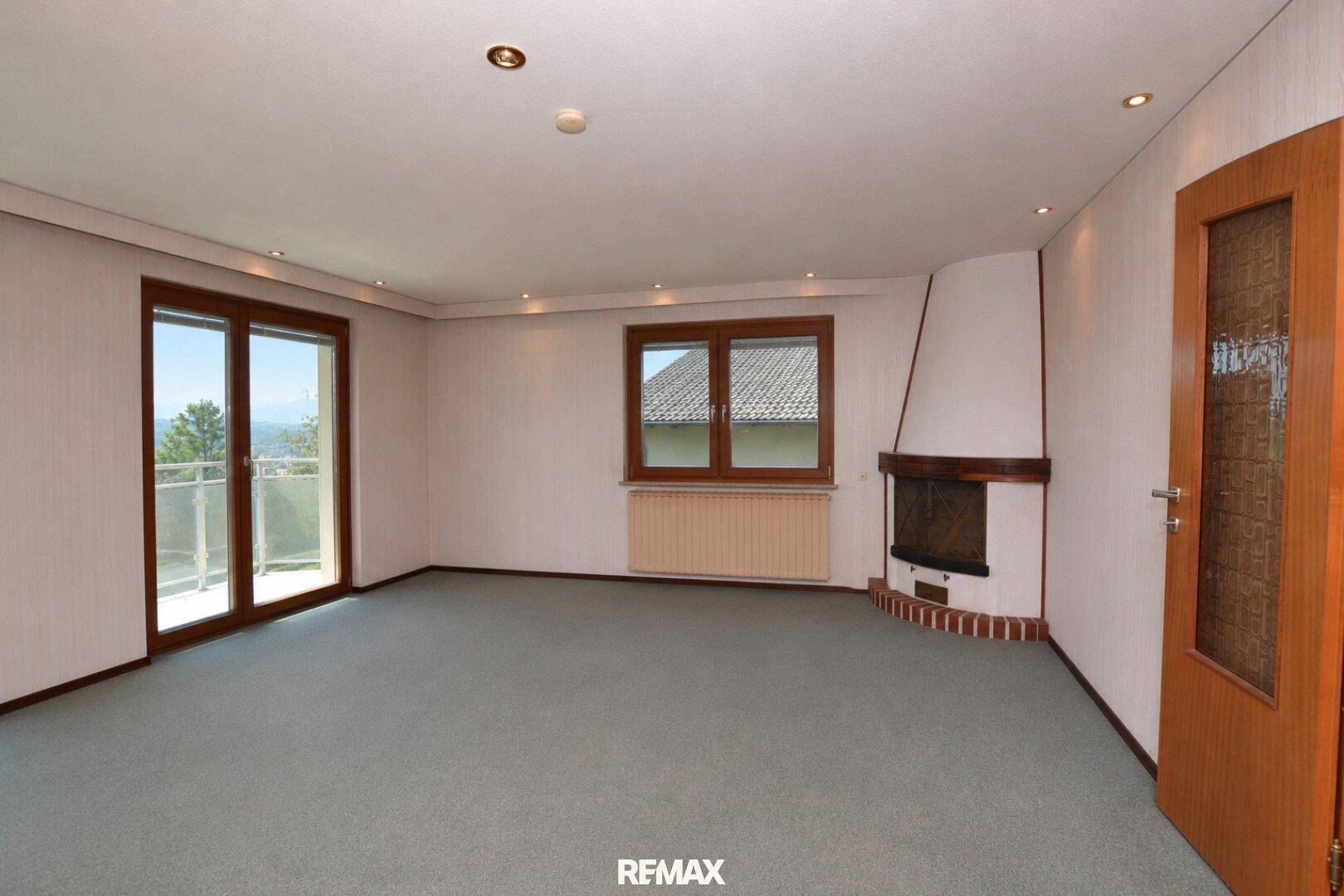 Geräumiges Wohnzimmer mit Kamin, Teppichboden und Zugang zu einem Balkon mit schöner Aussicht.