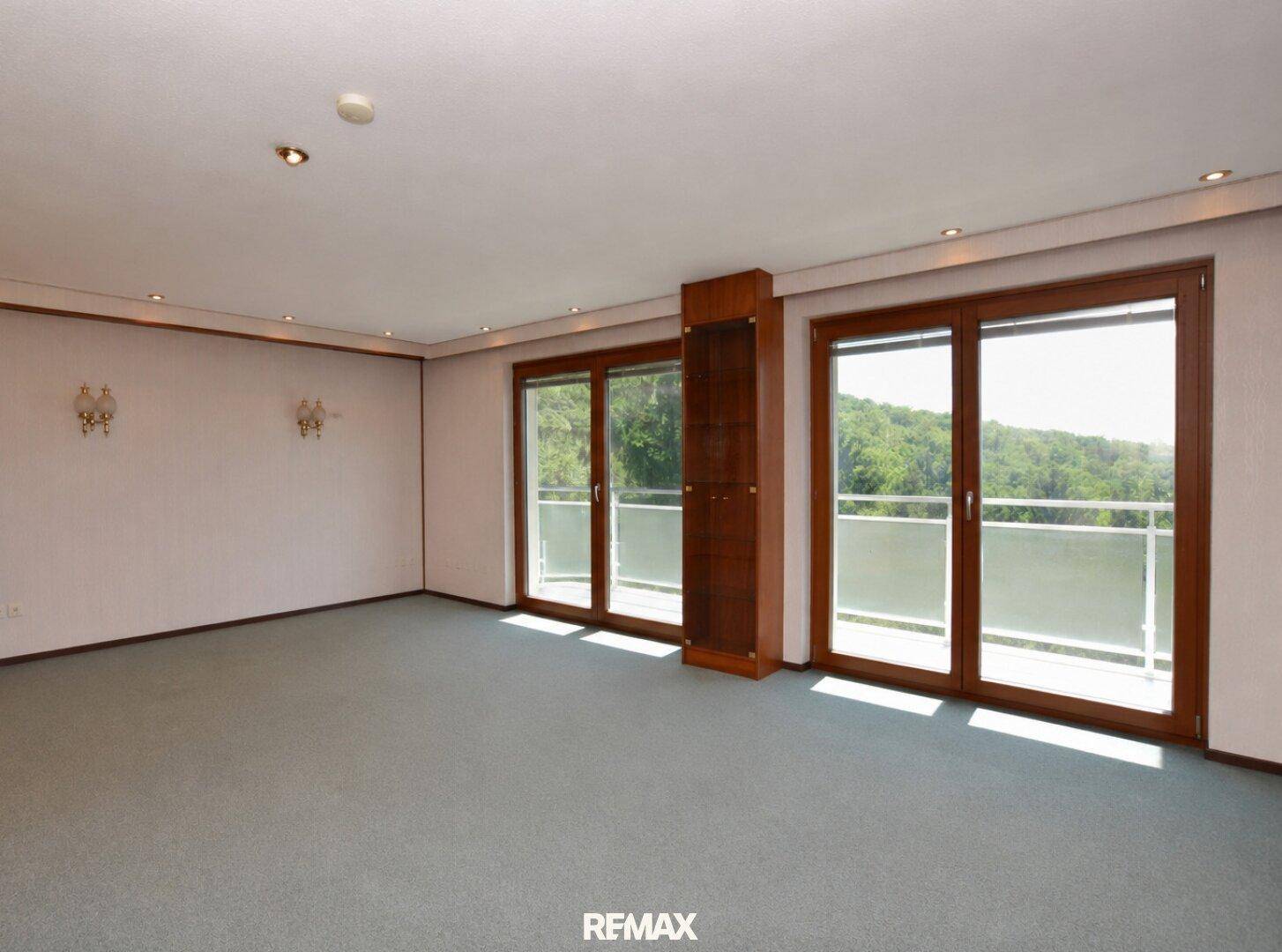 Heller Wohnbereich mit großen Fenstern, die viel Tageslicht hereinlassen und Zugang zum Balkon bieten.