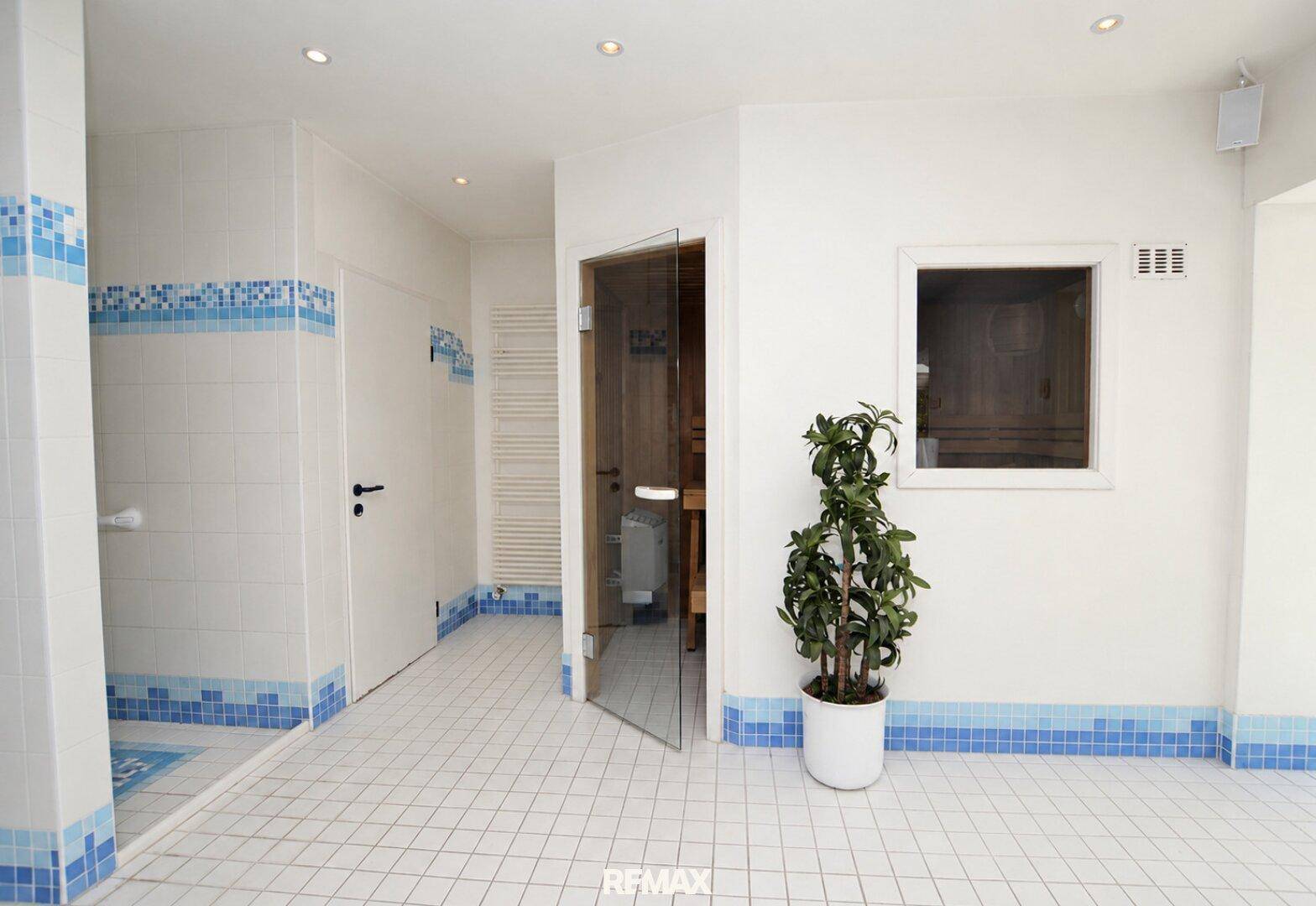 Wellnessbereich mit Zugang zur Sauna, Duschbereich und hellen Fliesen, angrenzend an den Pool.