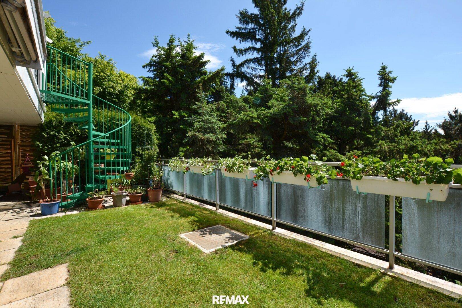 Grüner Gartenbereich mit Rasen, Pflanzen in Kübeln und einer auffälligen grünen Wendeltreppe.