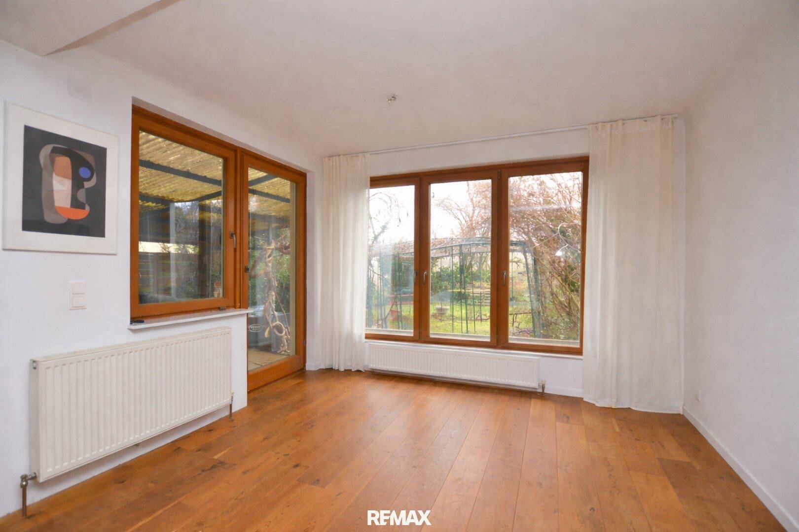 Heller Raum mit Holzboden, großen Fenstern und Zugang zum Gartenbereich.