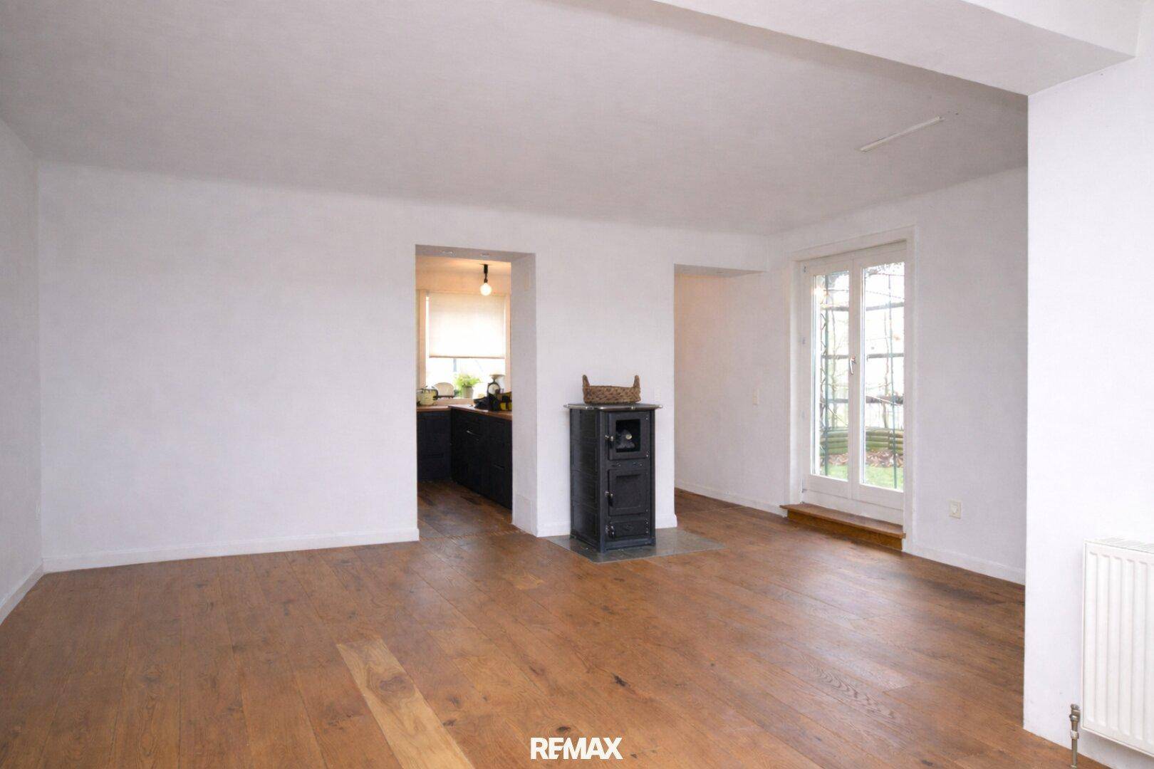 Geräumiger Wohnbereich mit Holzboden, Kaminofen und Zugang zu angrenzenden Räumen.