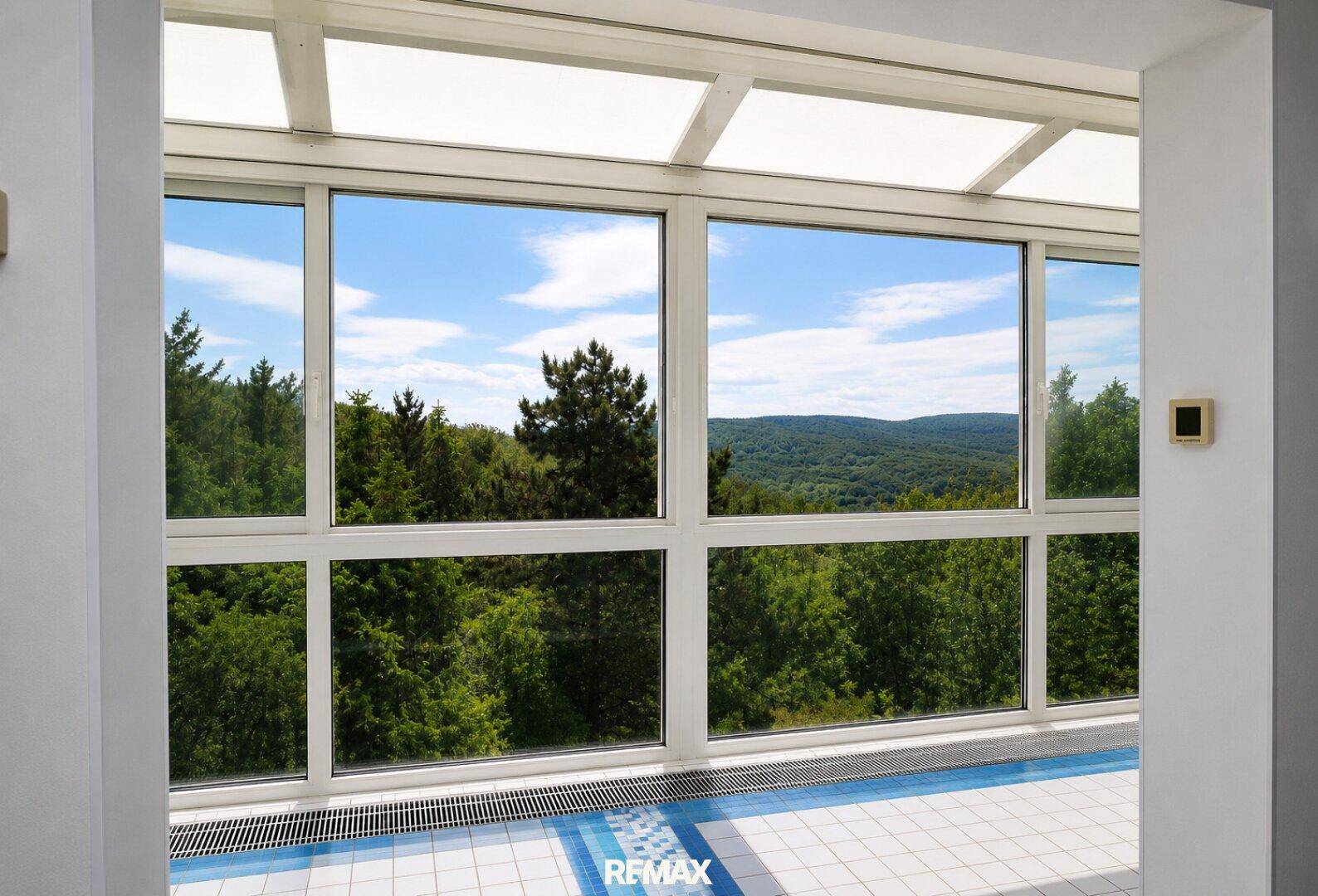 Panoramablick aus dem verglasten Poolbereich auf die umliegende grüne Waldlandschaft.