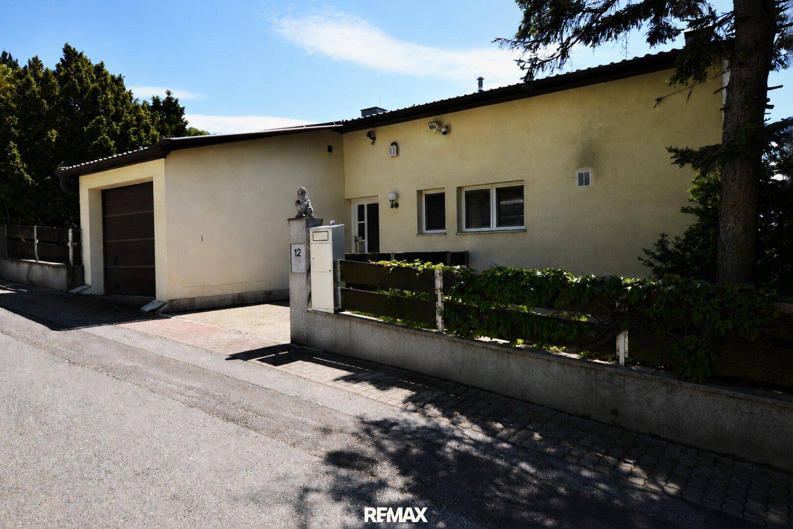 Vorderansicht eines Hauses mit integrierter Garage und einer gepflasterten Einfahrt von der Straße aus.