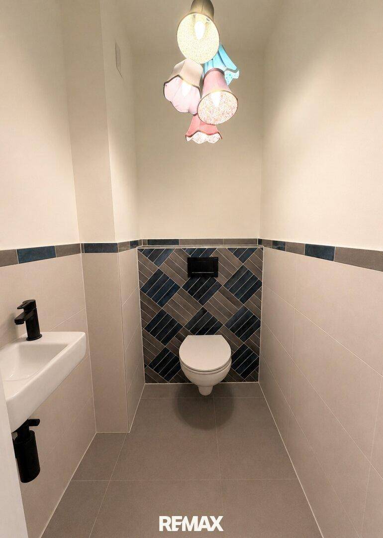 Modernes Gäste-WC mit Wand-WC, kleinem Waschbecken und dekorativen Fliesen.