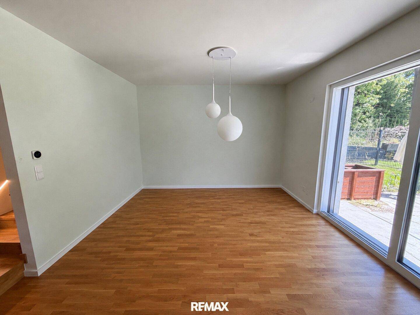 Geräumiger, leerer Raum mit Holzboden und großen Fenstern zum Garten, ideal für einen Essbereich.