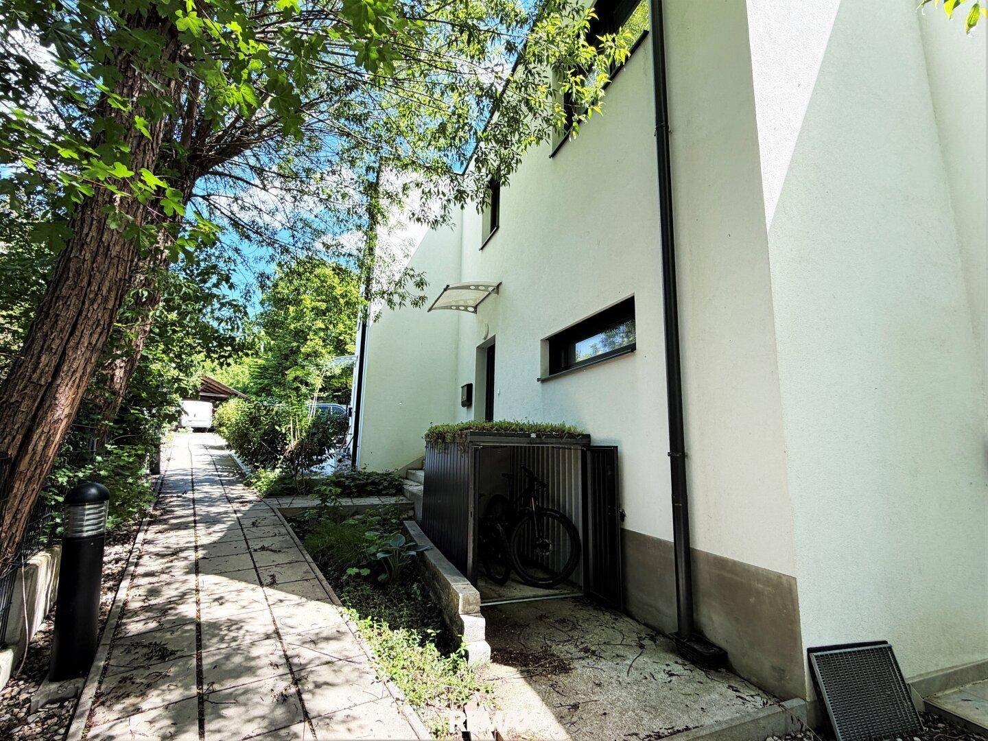 Seitenansicht des Hauses mit Fahrradunterstand und grünem Weg.