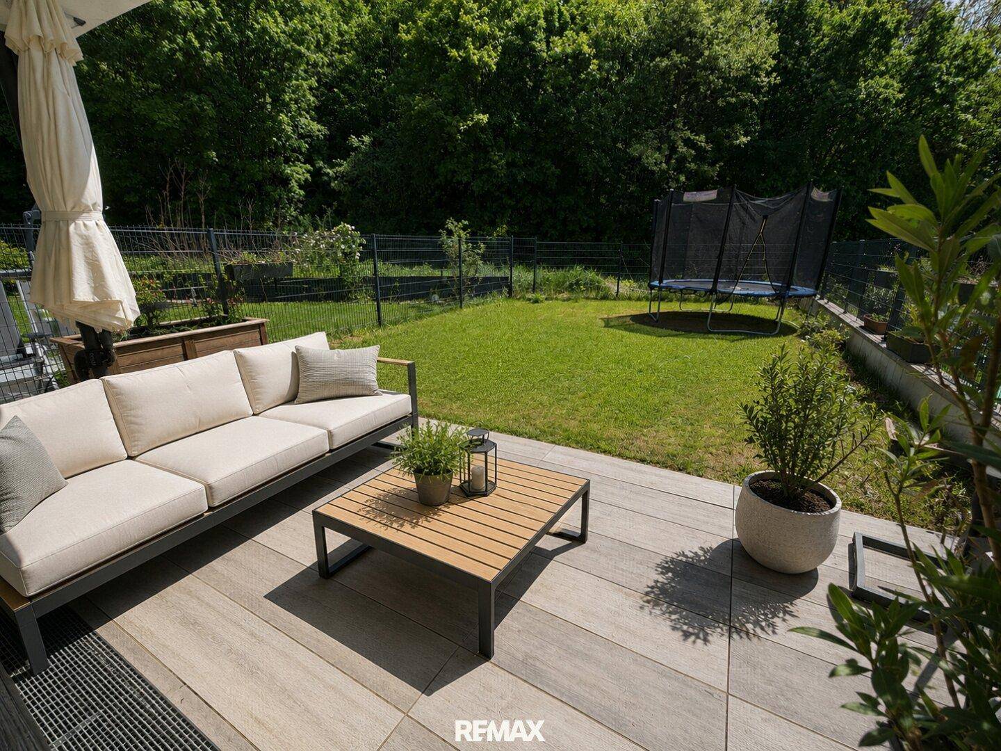 Moderne Terrasse mit Lounge-Möbeln und direktem Zugang zum Garten mit Trampolin.