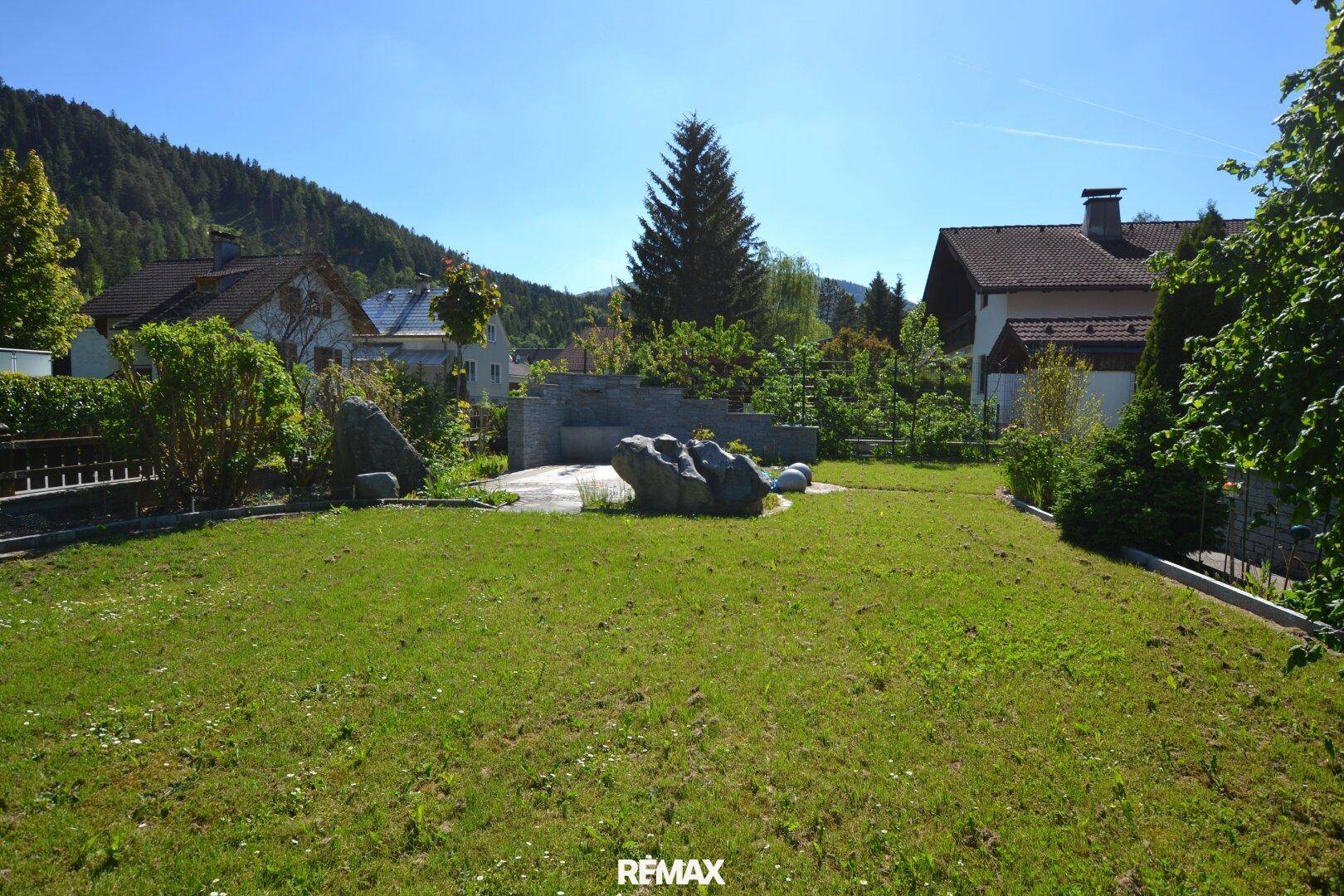 Großer, gepflegter Garten mit Rasenfläche, dekorativen Steinen und Bergblick.