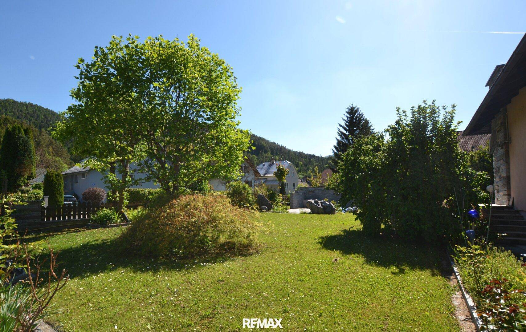 Hinterer Gartenbereich mit großem Baum, Rasenfläche und Blick auf die Umgebung.