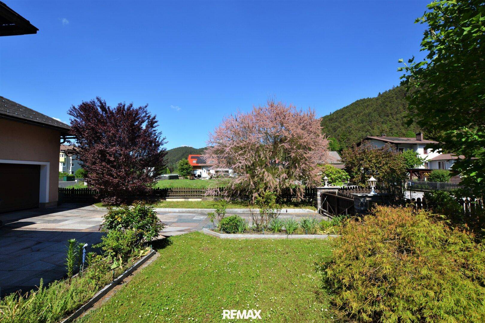 Vorderer Gartenbereich mit Rasen, blühenden Bäumen und Blick auf die Nachbarschaft.