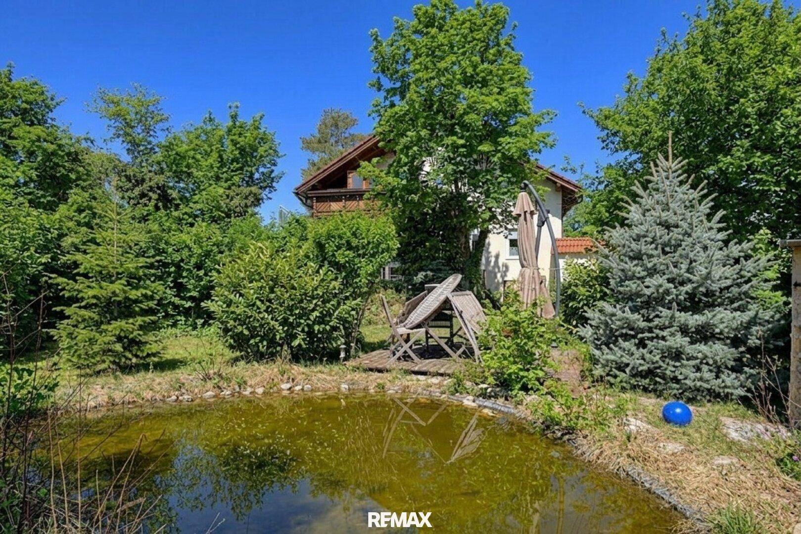 Idyllisches Einfamilienhaus mit Teich im Garten und Sitzgelegenheiten im Grünen.